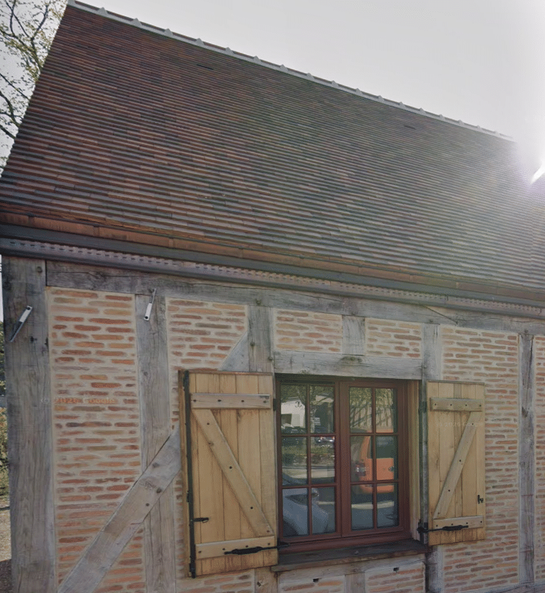 Façade d’une extension bois avec colombage apparent, briques et couverture en tuiles anciennes.