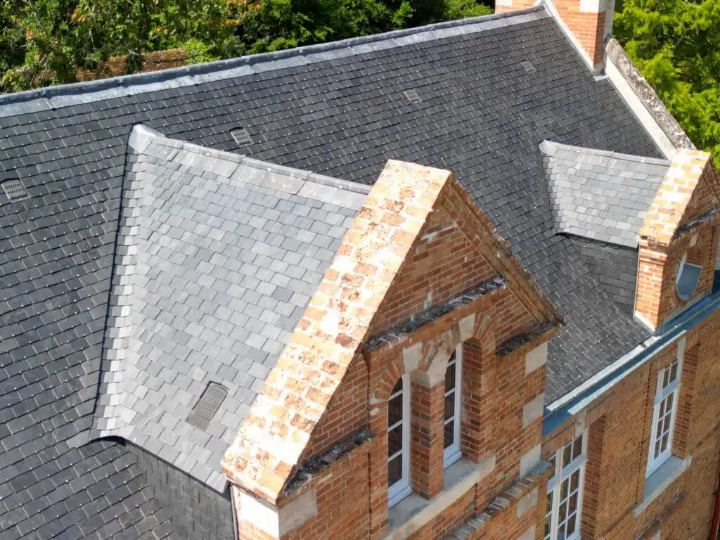 Toiture en ardoise avec plusieurs versants et lucarnes en briques sur une demeure ancienne