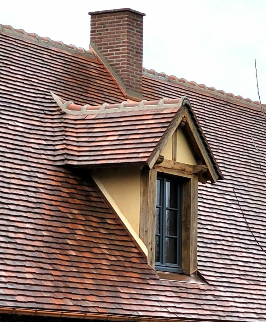 Toiture ancienne en tuiles plates avec lucarne, cheminée en briques et gouttière en cuivre